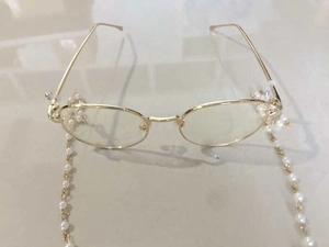 Close-up of golden metal eyeglass chain with white pearls on a minimalist optical frame