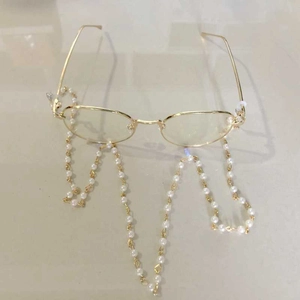 Detail of a gold circular frame glasses with a delicate white pearl decorative chain