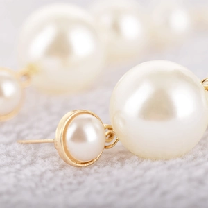 Macro shot of elegant cream-colored pearls and gold-plated metal base on drop earrings