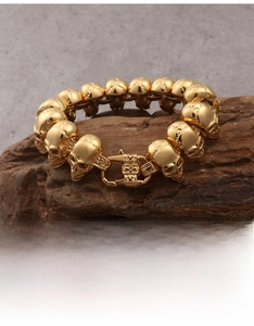 Detailed view of a gold skull link bracelet in stainless steel on dark wood base