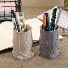 Detail view of beige and gray carved plastic pen holders on a desk with office accessories