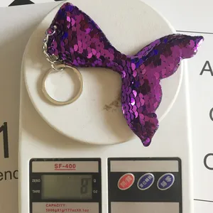 Detailed view of purple mermaid tail sequin keychain showing 8g weight on a scale