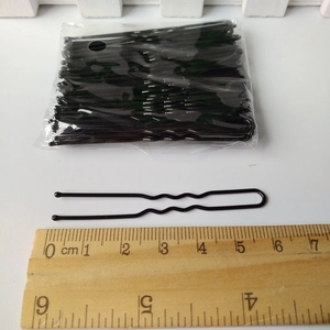Détail d'une épingle à cheveux noire en U de 6 cm mesurée avec une règle en bois