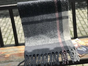 Detail of thick plaid scarf with soft tassels resting on an outdoor wooden bench