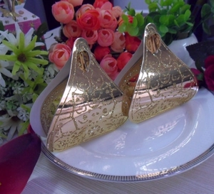 Close-up of golden triangle wedding favor boxes with hollow patterns on a ceramic plate
