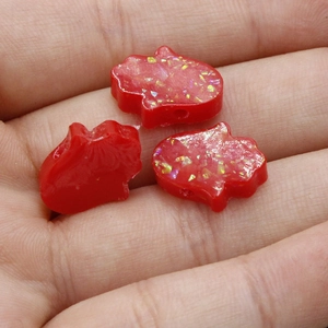 Detailed view of three red Hamsa hand resin charms with glitter on a palm for size scale
