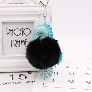 Close-up of cute seahorse keychain with black fluffy fur pom and blue faux leather