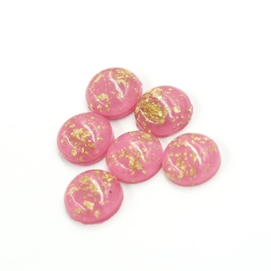 Detail of six 12mm pink synthetic opal resin cabochons with gold foil flakes on white base