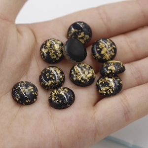 Close-up of 12mm round black resin cabochons with gold foil flakes in a palm