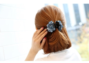 Blue fabric flower hair claw clip worn by a model in a bright indoor setting