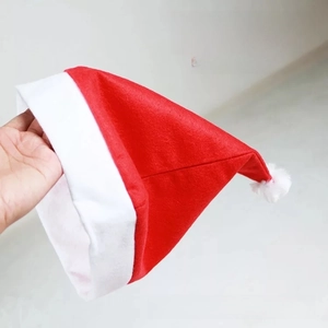Detail of red non-woven Christmas hat with white pompom held in hand for festive attire