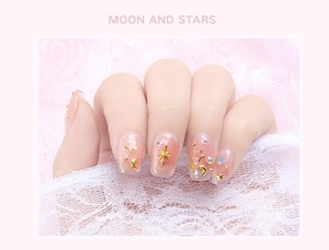 Detailed view of gold moon and star nail charms with rhinestones on white lace