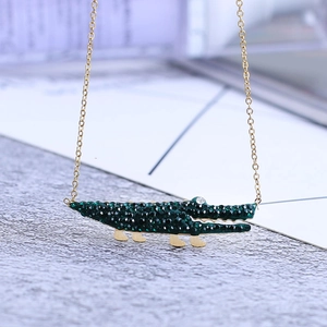 Gros plan du collier doré avec pendentif crocodile mignon serti de strass verts