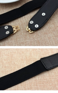 Detail of black elastic belt with gold metal interlocking buckle and faux leather finish