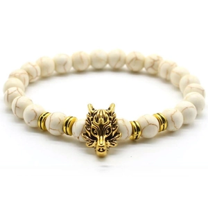 Detail shot of white stone beads with a golden metal wolf head charm on an elastic bracelet