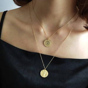 Detail of layered gold coin pendant necklaces worn on neck with vintage textured medallions