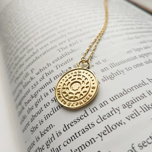 Detail of gold coin pendant with LIVE TO EXPRESS engraving on an open vintage book page