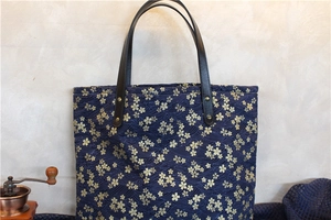 Détail macro du sac cabas en toile bleu marine avec motifs cerisiers dorés et anses en cuir