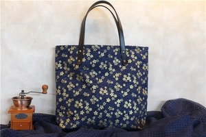 Détail d'un sac en toile bleu marine avec motifs de cerisiers et anses en cuir