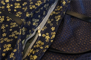 Macro des imprimés cerisiers dorés et de la fermeture éclair sur un sac fourre-tout bleu
