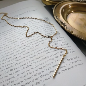 Detail of a minimalist gold flat link chain necklace with a solid bar pendant on a book