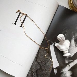 Detail of a minimalist gold Y-shaped necklace with a long bar pendant on a book