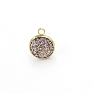 Close-up of circular gold resin pendant with pink glitter texture and small hanging loop