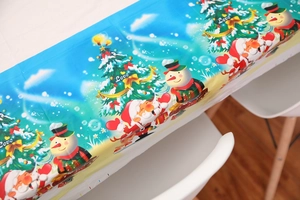 Detail of Christmas tablecloth featuring Santa, snowman, and tree patterns on a white table