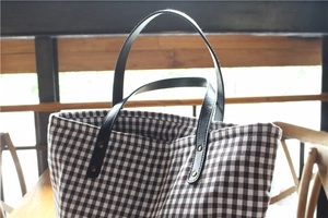Detail of vintage plaid tote bag featuring black leather straps and gold rivets