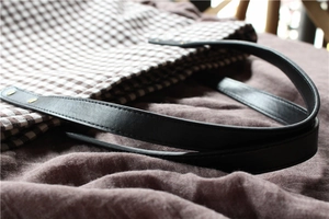 Detail of gingham canvas tote bag with black leather handle and golden rivet accents