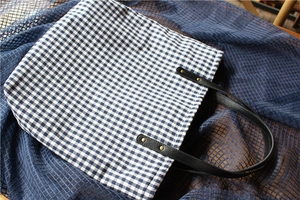 Detailed texture of black and white checkered canvas tote with leather handle and rivets