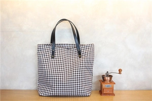 Detail of checkered tote bag with leather straps next to vintage coffee grinder