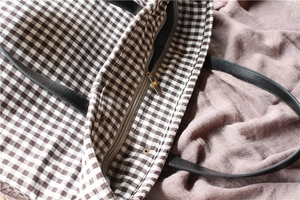 Close-up of metal zipper and leather strap on a brown checked canvas tote bag