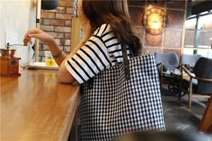 Detailed view of checkered canvas tote bag with black leather straps and metal rivets