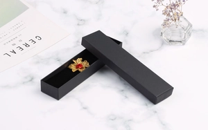 Close-up of a black rectangular jewelry box with a gold flower brooch on marble background