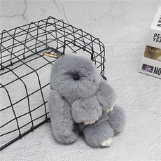 Detail of dark grey mink fur rabbit keychain with golden clasp on metal mesh background