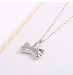 Macro shot of silver bone-shaped cremation urn pendant with black paw prints and screw cap