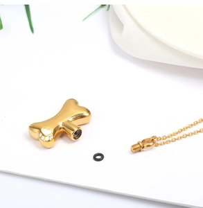 Detailed close-up of golden bone cremation pendant with threaded top and small paw print detail