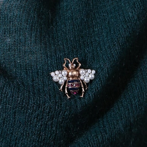 Vintage gold bee brooch with white pearls and blue enamel on green fabric background