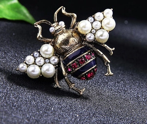 Macro detail of bee brooch with pearls and red crystals on black textured background