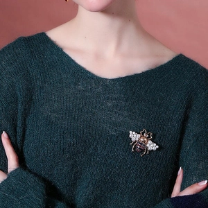 Vintage gold-tone bee brooch with pearls and glitter details on green knitwear