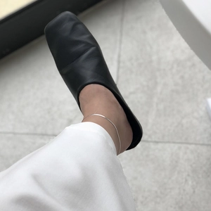 Close-up of minimalist S925 sterling silver blade chain anklet worn with black flat shoes