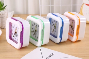 Four colorful square quartz alarm clocks in purple, green, blue and orange on a wood desk