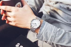 Detail of silver Milanese mesh watch strap on wrist holding a coffee cup