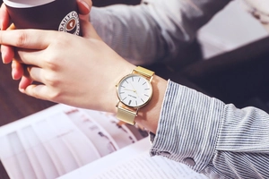 Detail of minimalist gold mesh strap watch with white dial on woman's wrist