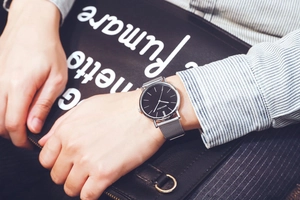 Close-up of minimalist silver mesh watch with black dial worn by man in business setting
