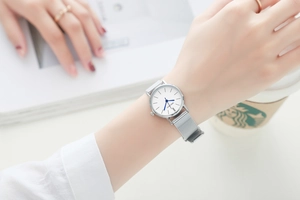 Detailed shot of women's silver mesh watch featuring white dial and blue hands