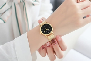 Close-up of minimalist gold mesh strap watch with black dial worn on a female wrist