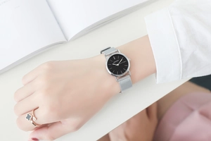 Close-up of silver mesh strap watch on wrist with a minimalist black dial and clover ring