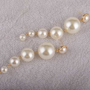 Detail showing five white gradient pearls on golden metal elegant long dangle earrings